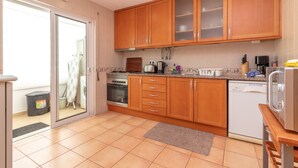A modern kitchen with wooden cabinets, stainless steel appliances, and a sliding glass door leading to a laundry area. - Casa Amiga - Communal pool & garden, just 500m from beach (Carvoeiro)