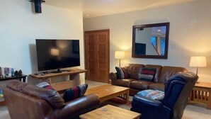 A living room with a television, leather sofas, a coffee table, and a wooden cabinet.