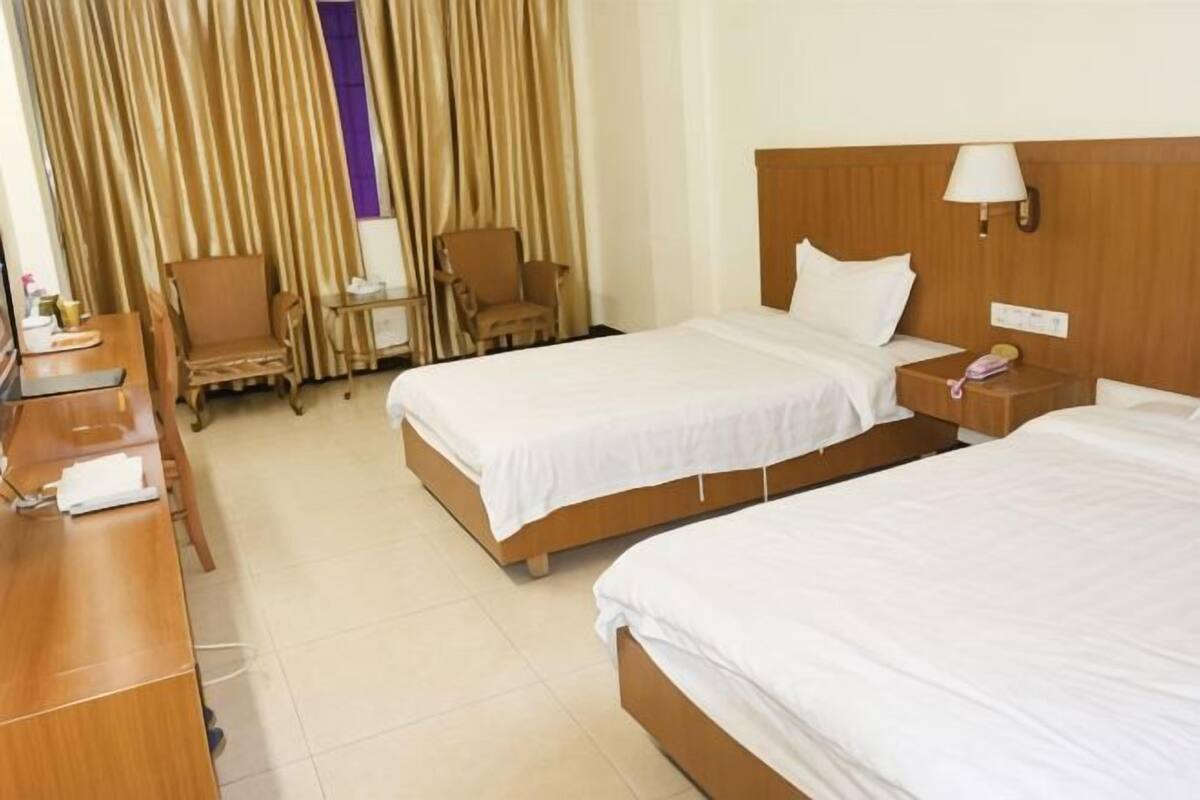 Una habitación de hotel con dos camas, un escritorio, sillas, una lámpara y cortinas.