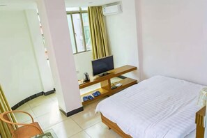 Een hotelkamer met een bed, een televisie op een houten standaard, een stoel en een raam met gordijnen.