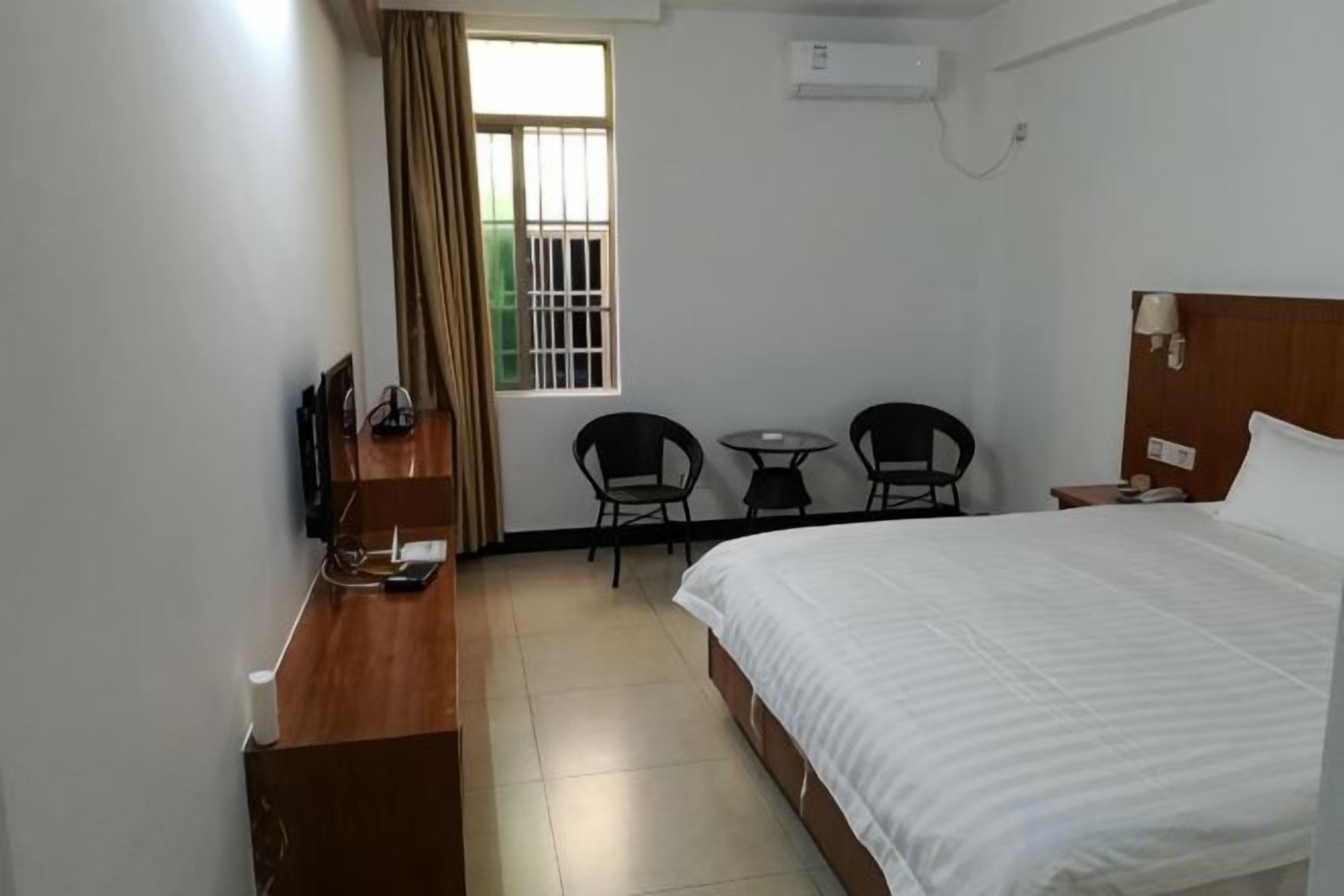 Una habitación de hotel con cama, escritorio, silla, mesita y ventana con cortinas.