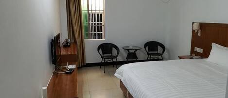 Una habitación de hotel con cama, escritorio, silla, mesita y ventana con cortinas.