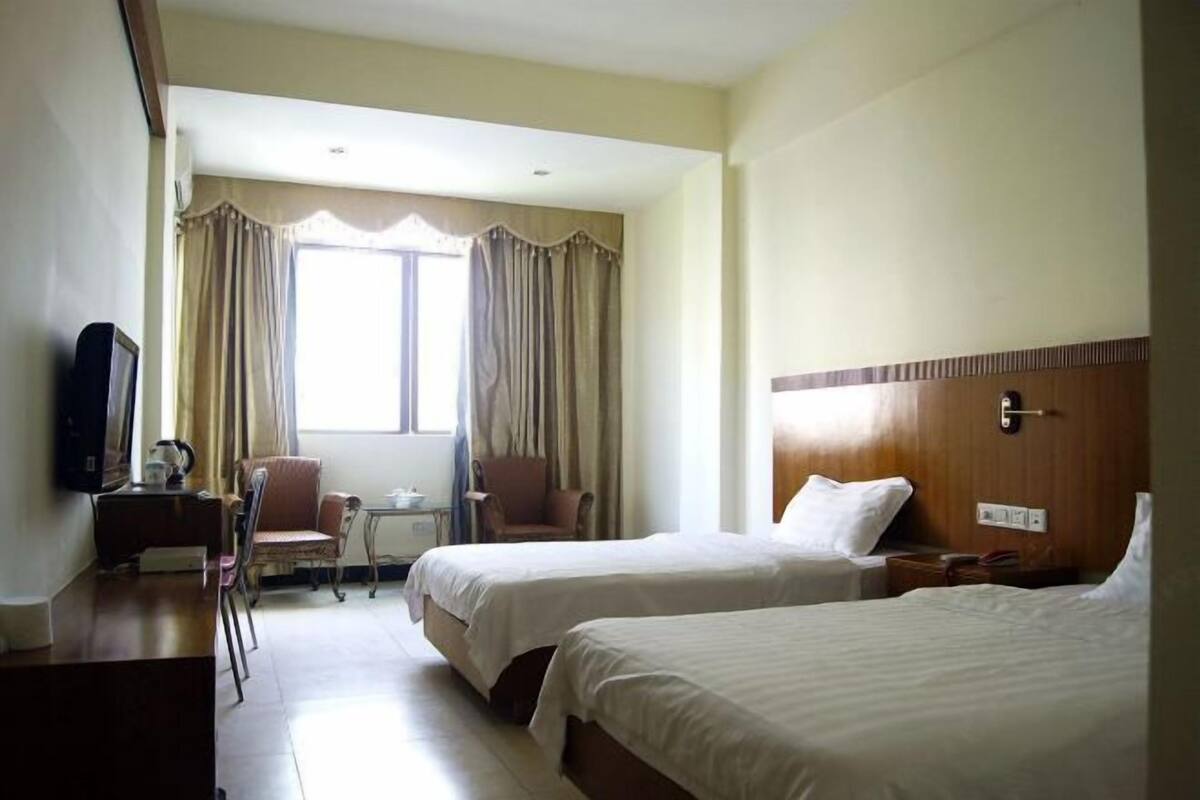Habitación de hotel con dos camas, un escritorio, una silla y un televisor.