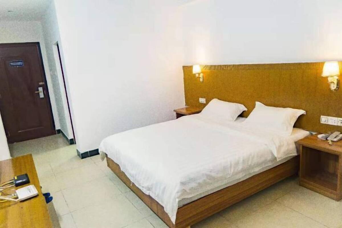 Una habitación de hotel con cama de madera, ropa de cama blanca, dos lámparas de noche y un teléfono junto a la cama.