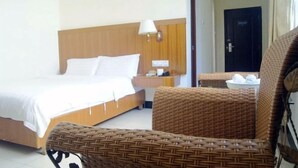Camera d'albergo con un letto, un comodino, una lampada, una sedia in vimini e una porta per il bagno.