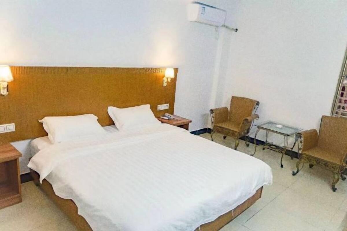 Habitación de hotel con una cama grande, dos mesitas de noche, una pequeña mesa con sillas y un aire acondicionado instalado en la pared.