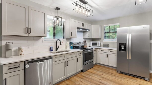 A modern kitchen with stainless steel appliances, white cabinetry, and a wooden floor. - 3 miles from NAS * King and Queen Bed * Covered Patio * Luxury Bath * Open concept Living (Pensacola)