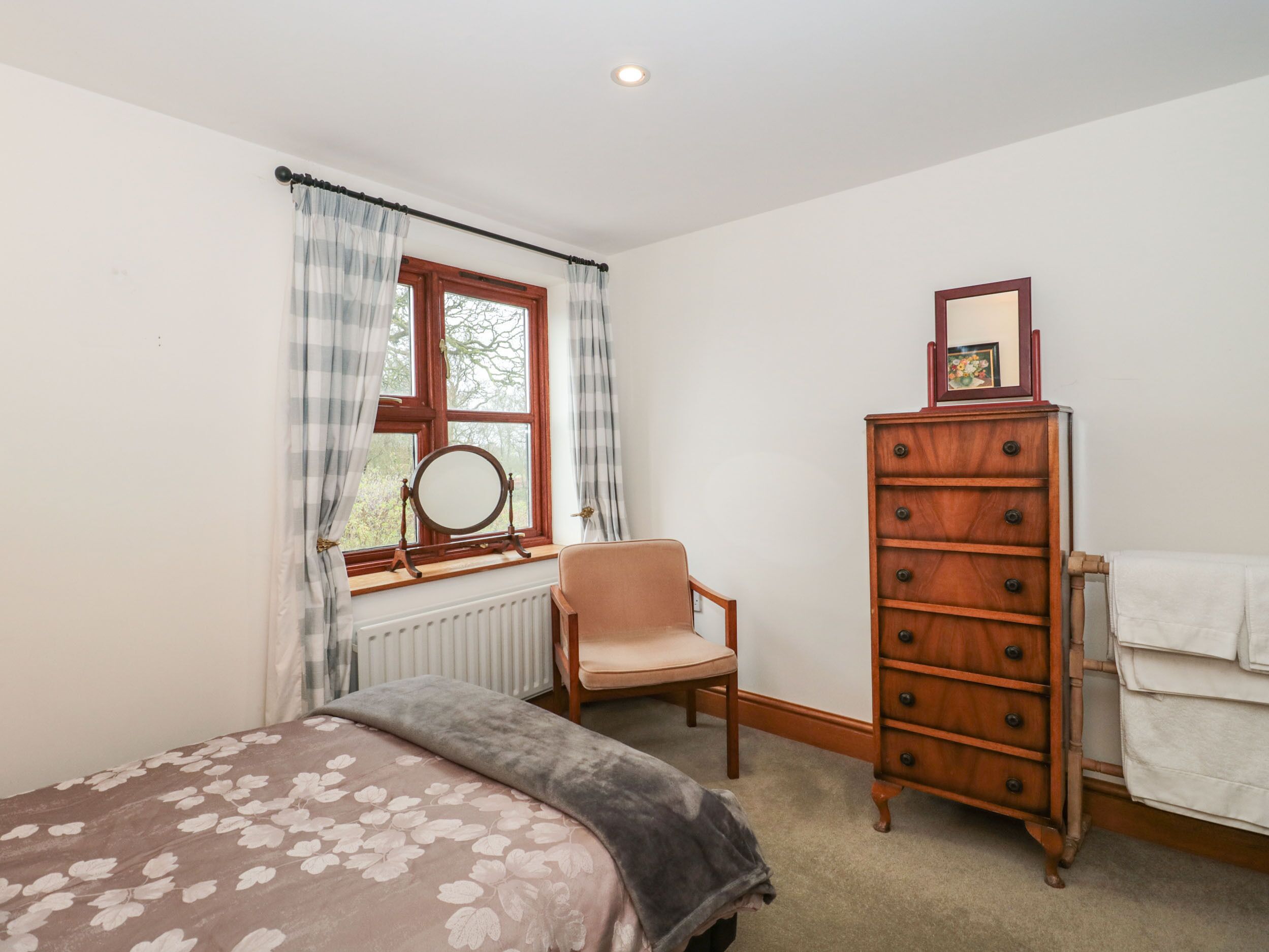 A bedroom with a bed, a chair, a dresser, a window with curtains, and a radiator.