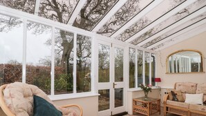 Une pièce chaleureuse avec une grande fenêtre, des meubles en osier, un miroir et un tapis à motifs.