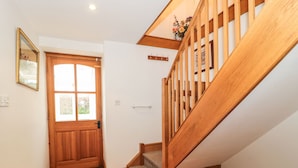 Un escalier en bois avec une rampe, une porte en bois avec des panneaux de verre et un petit tapis sur le sol.