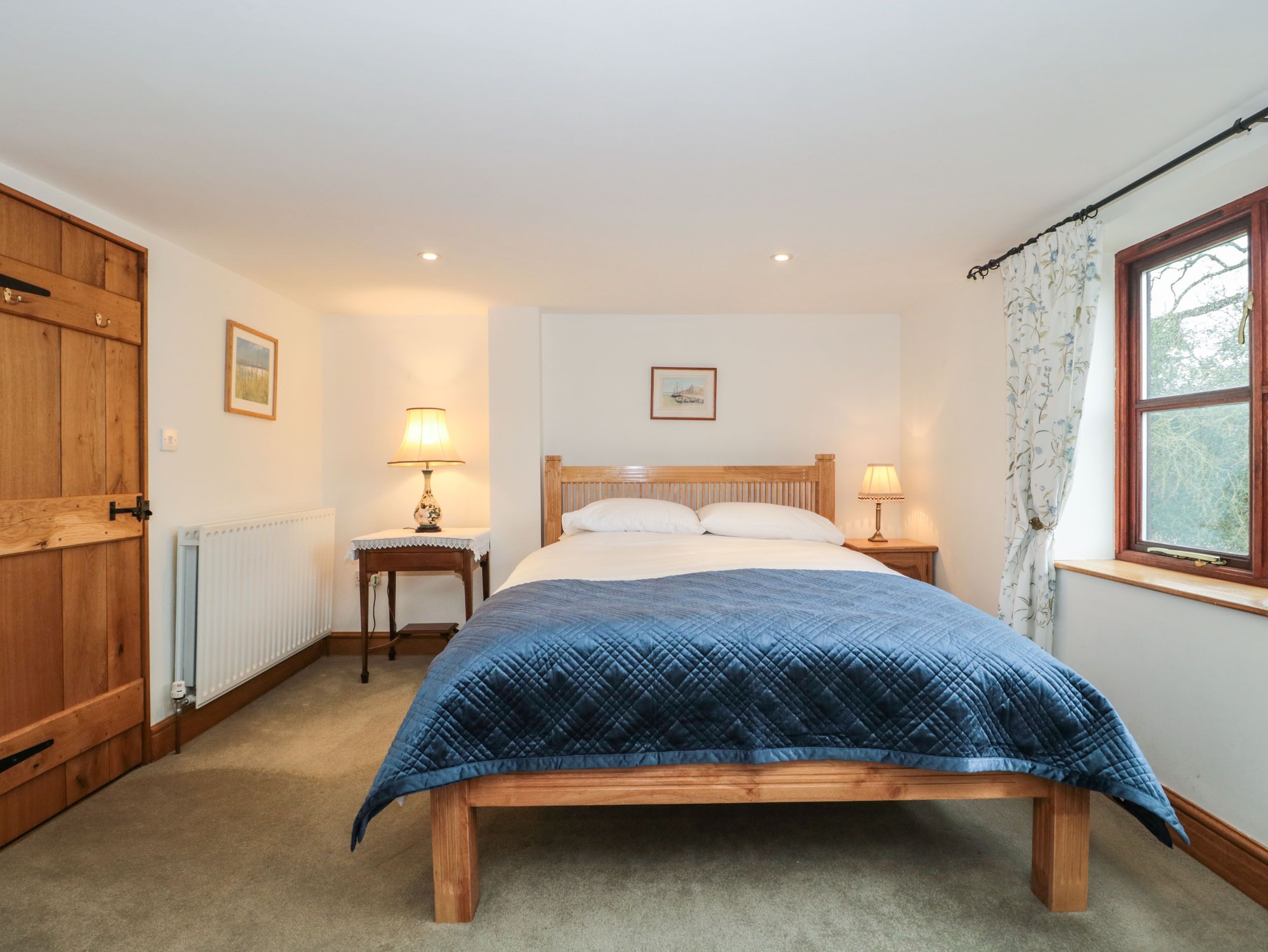 Une chambre à coucher avec un lit en bois, deux tables de chevet avec des lampes, un radiateur et une fenêtre avec des rideaux.