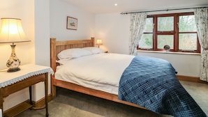 Une chambre avec un lit en bois, une table de chevet avec une lampe, une fenêtre avec des rideaux et un tableau au mur.