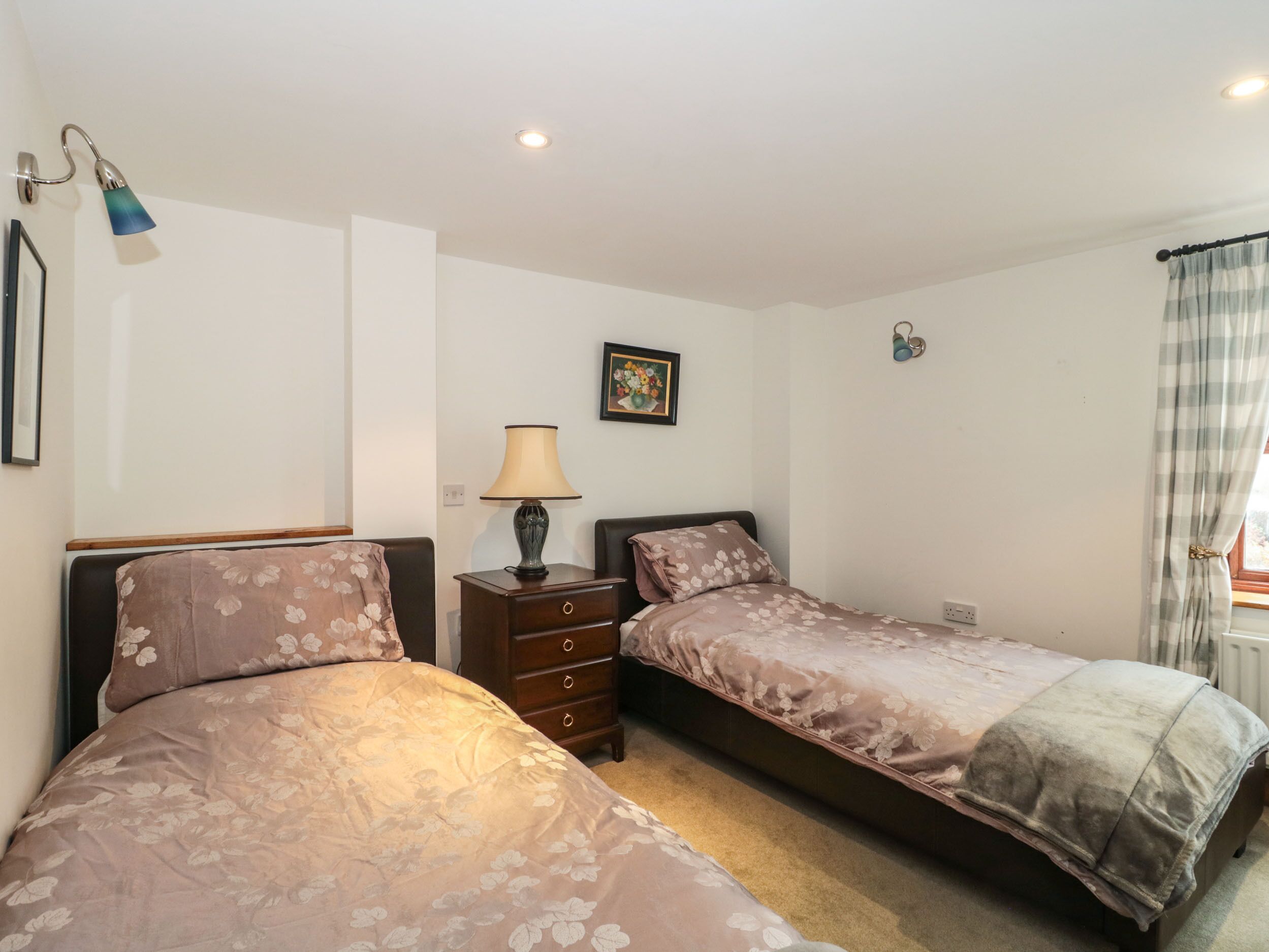 A bedroom with two beds, a nightstand with a lamp, a framed picture on the wall, and a window with curtains.