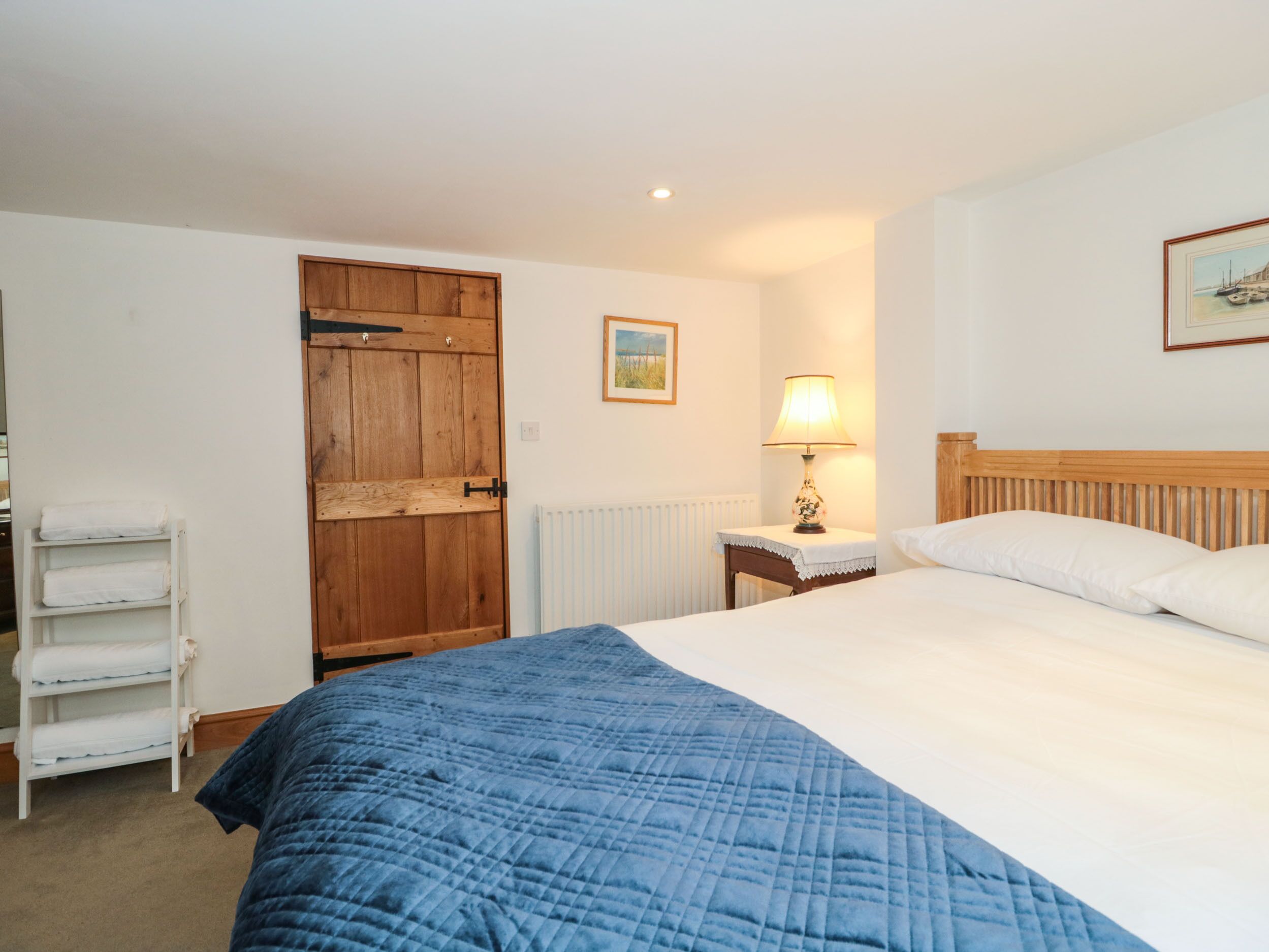 A bedroom with a bed, a wooden door, a white radiator, a bedside table with a lamp, and a framed picture on the wall.