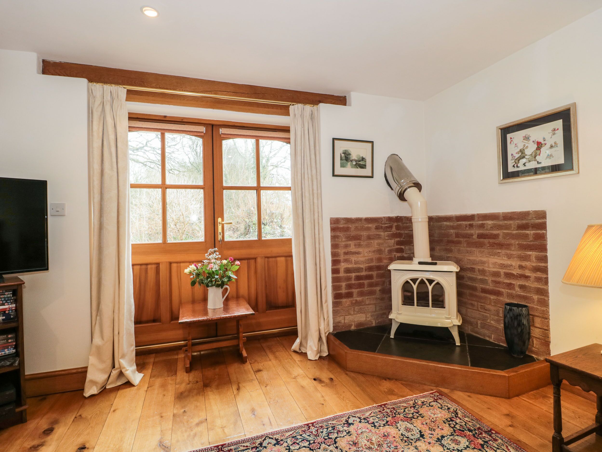 Una sala de estar acogedora con suelo de madera, chimenea, televisión y ventana con cortinas.