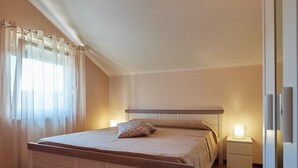 Un dormitorio con una cama de madera, una mesita de noche, una alfombra mullida y una ventana con cortinas de gasa.
