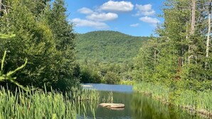 A serene lake surrounded by lush greenery and trees. - Glamping Retreat with private lake, 330+ acres and frontage on the Cedar River (Indian Lake)