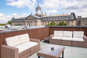 Une terrasse sur le toit, aménagée avec des meubles en osier et une table, d’où l’on peut admirer un bâtiment historique surmonté d’un dôme.