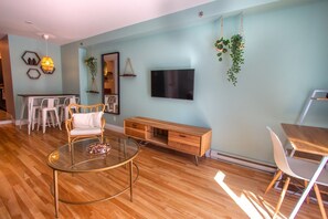 Un salon moderne avec une table basse en verre, un canapé blanc, un meuble TV en bois et un coin repas avec une table et des chaises blanches.