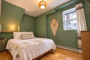 Une chambre à coucher avec un lit, une table de chevet, une décoration murale et une fenêtre avec des rideaux.