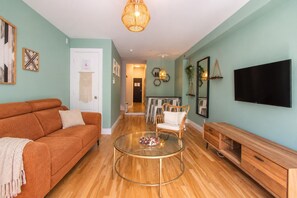 Un salon comprenant un canapé, une table basse ronde en verre, un téléviseur et un meuble en bois.