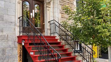 A building with a stone facade, a wooden door with the number 3602, and a red staircase with black railings.