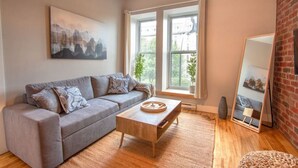 A modern living room with a grey sofa, a wooden coffee table, and a large window with white curtains. - Zen/Rooftop/Terraces/Plateau/St-Denis/AC/TV (Montréal)