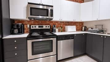 Una cocina moderna con electrodomésticos de acero inoxidable, armarios blancos y una pared de ladrillo.