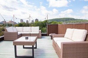 Terraço no telhado com móveis de vime, mesa de vidro e vista para a cidade.