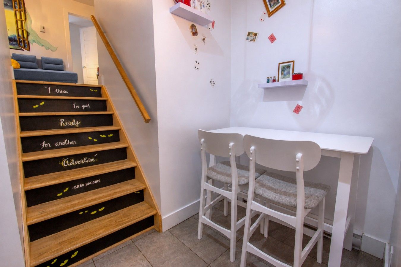 Un escalier dont les marches sont ornées de phrases motivantes, un bureau blanc avec deux chaises et un mur décoré de cartes et de photos.