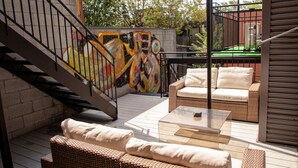 Un patio con mobiliario de mimbre, una mesa de vidrio y un mural en la pared.