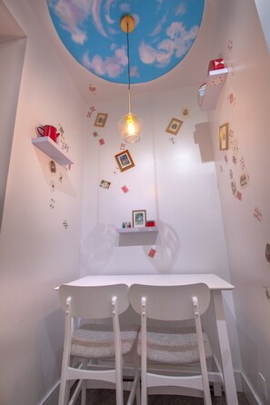 Une pièce avec une table et des chaises blanches, une fresque au plafond et des décorations murales comprenant des cartes et des images.