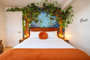 Une chambre à coucher avec un lit, une tête de lit ornée d’une fresque représentant un arbre, deux lampes de chevet et un mur sur lequel est écrit le mot « ONCE ».