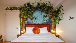 Un dormitorio con una cama, cabecera de madera, dos lámparas de noche y una pared con un mural de un árbol.