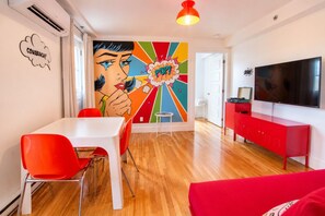 A modern living room with a vibrant pop art mural, a flat-screen TV, a red cabinet, and a dining area with red chairs. - Pop/Rooftop/Terraces/Plateau/St-Denis/AC/TV (Montréal)