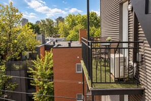 A rooftop terrace with a view of a cityscape, a brick building, and a modern structure with a balcony.