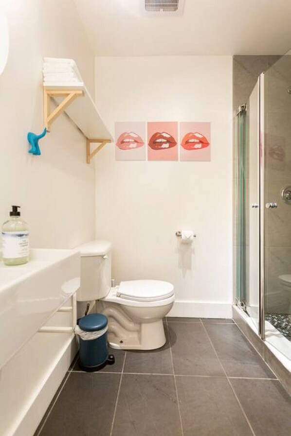 A bathroom with a toilet, a shower, and a sink. There are three pictures of lips on the wall. - Pop/Rooftop/Terraces/Plateau/St-Denis/AC/TV (Montréal)