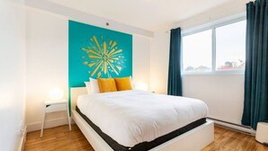 A modern bedroom with a bed, a teal accent wall, and a city view. - Pop/Rooftop/Terraces/Plateau/St-Denis/AC/TV (Montréal)