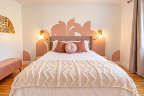 A neatly made bed with a patterned blanket, a headboard with a geometric design, and wall-mounted lighting.