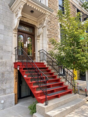 A building with a stone facade, a wooden door with the number 3602, and a red staircase with black railings. - Gatsby/Rooftop/Terraces/Plateau/St-Denis/AC/TV (Montréal)