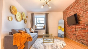 A modern living room with a grey sofa, a round coffee table, and a brick wall. - Gatsby/Rooftop/Terraces/Plateau/St-Denis/AC/TV (Montréal)
