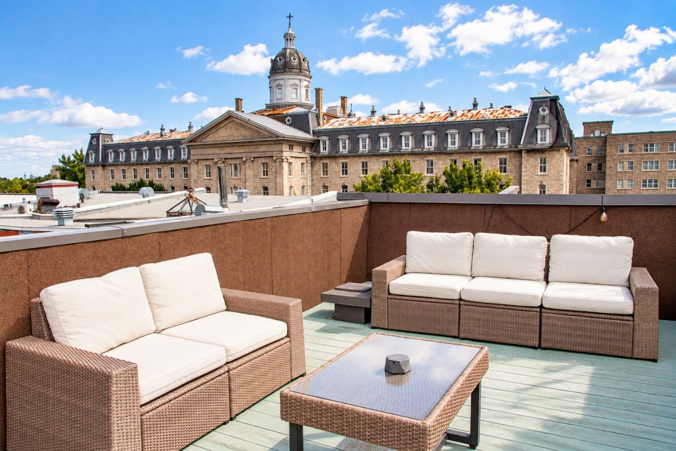 A rooftop terrace with wicker furniture, a table, and a view of historic buildings.