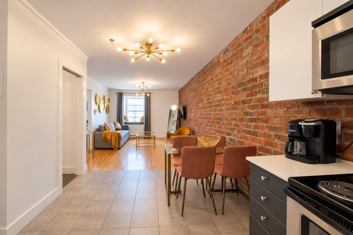 A modern kitchen with a brick wall, a coffee maker, and a dining area with chairs.