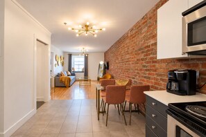 A modern kitchen with a brick wall, a coffee maker, and a dining area with chairs. - Gatsby/Rooftop/Terraces/Plateau/St-Denis/AC/TV (Montréal)
