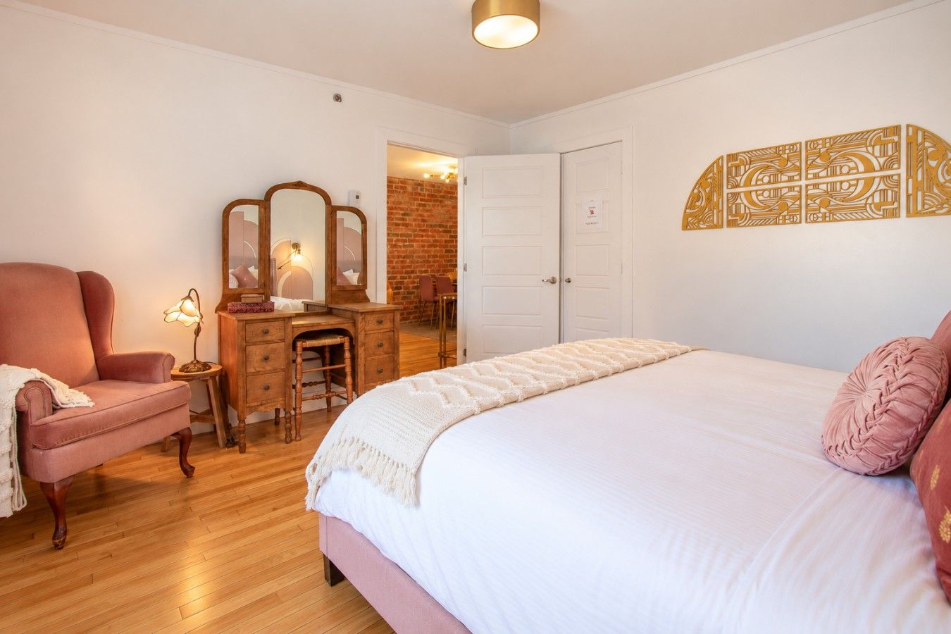 A bedroom with a large bed, a wooden dresser, a chair, and a mirror.
