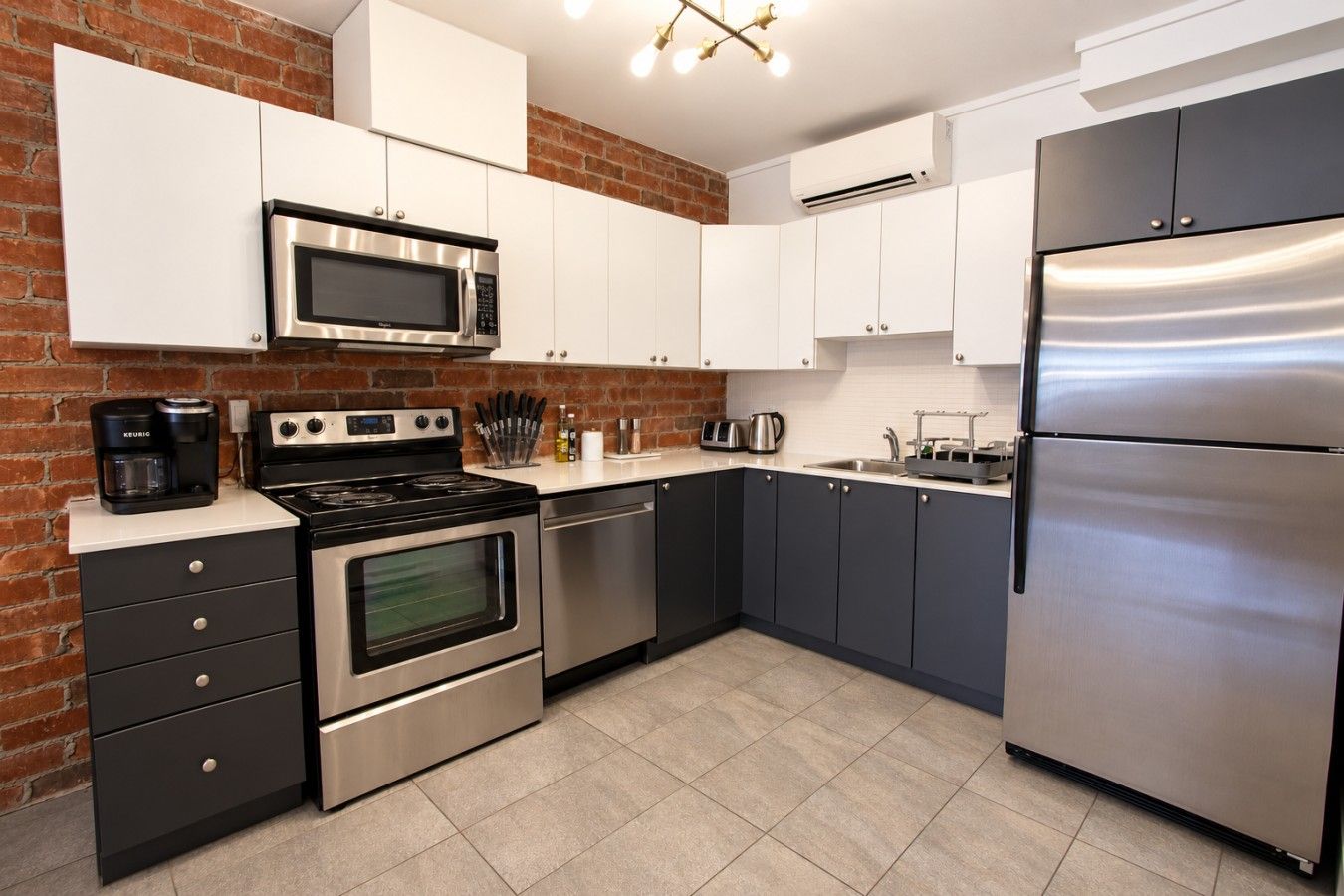 A modern kitchen with stainless steel appliances, white cabinetry, and a brick accent wall.