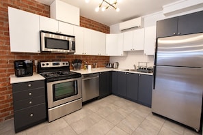 Una cocina moderna con electrodomésticos de acero inoxidable, armarios blancos y una pared decorativa de ladrillo.