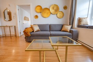 Ein stilvolles Wohnzimmer mit einem grauen Sofa, zwei Couchtischen mit Glasplatten und Wandbildern.