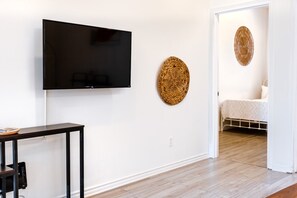 A room with a flat-screen TV mounted on the wall, a small table with a remote control, and a bed with a white blanket. - Africa/2Bdr/Plateau/St-Laurent/SelfCheck-In/AC/TV (Montréal)