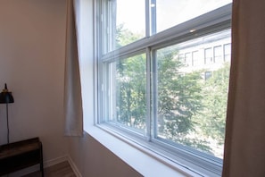 Enjoy a serene view of the tree-lined street from the large window, framed by white trim and a sheer curtain.